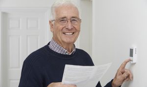 A man smiling whilst turning down his haetinga nd holding an energy bill
