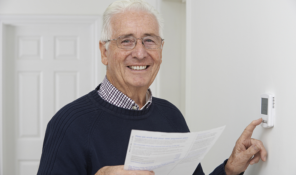 A man smiling whilst turning down his haetinga nd holding an energy bill