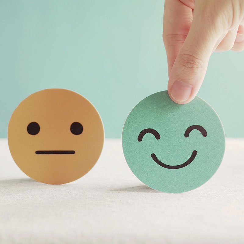 A yellow frowning face and a smiling green face, being held by two fingers